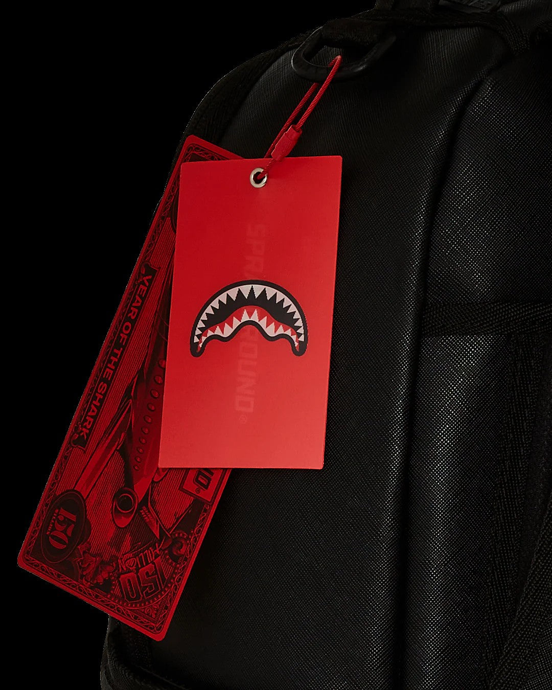 Black backpack with a red tag featuring a shark mouth logo on a black background