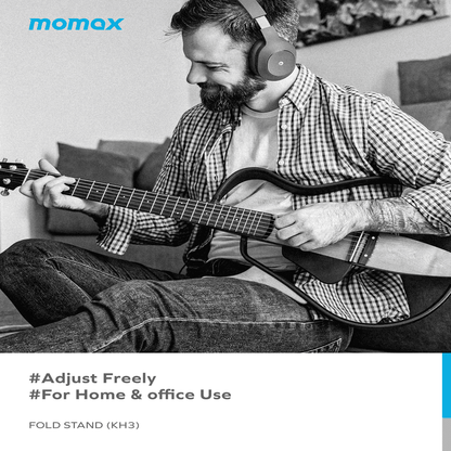Man playing guitar with headphones on, sitting on a couch with 'momax' branding.