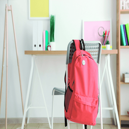 Pink backpack hanging on a chair in a room with shelves and decor.
