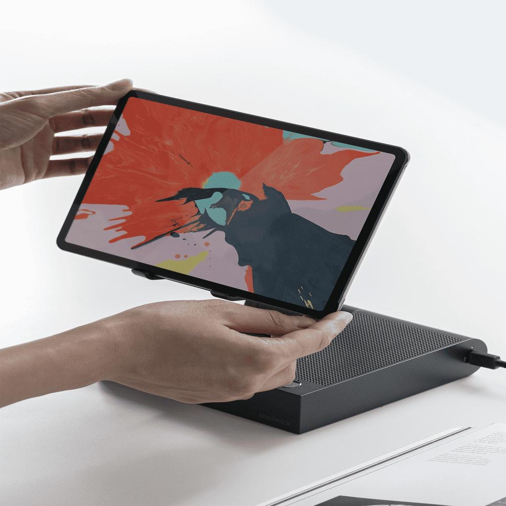 Person holding a tablet with a colorful display over a black electronic device on a white surface.