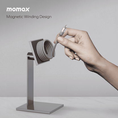 Hand interacting with a magnetic winding design product on a stand, with 'momax' branding.