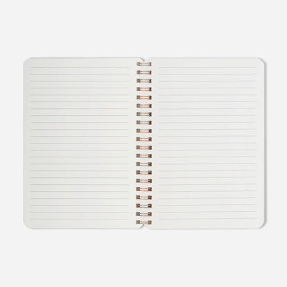 Open notebook with white pages and rose gold spiral binding on a light gray background