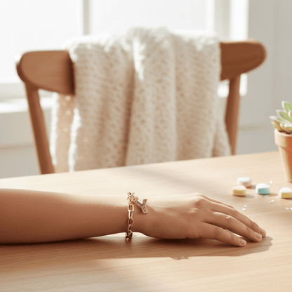 Hand wearing a bracelet on a wooden table with a chair and plant in the background