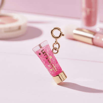 Pink lip gloss charm with gold accents on a light pink background