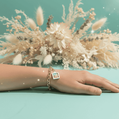 Hand wearing a bracelet with a charm on a light blue background with decorative plants.