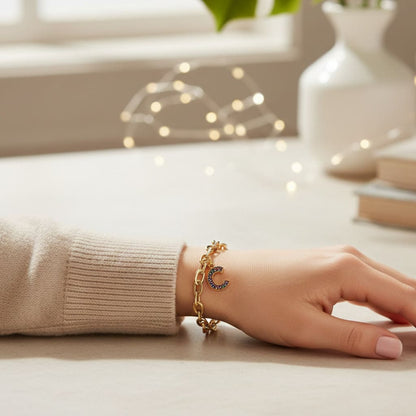 Hand wearing a gold bracelet with a moon charm on a light surface.