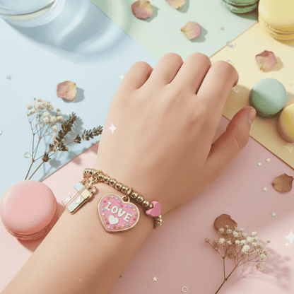 Hand wearing a gold bracelet with a pink heart charm labeled 'LOVE' on a colorful background with macarons and flowers.
