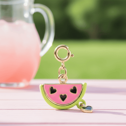 Watermelon-shaped keychain with black heart designs on a pink surface with a blurred background