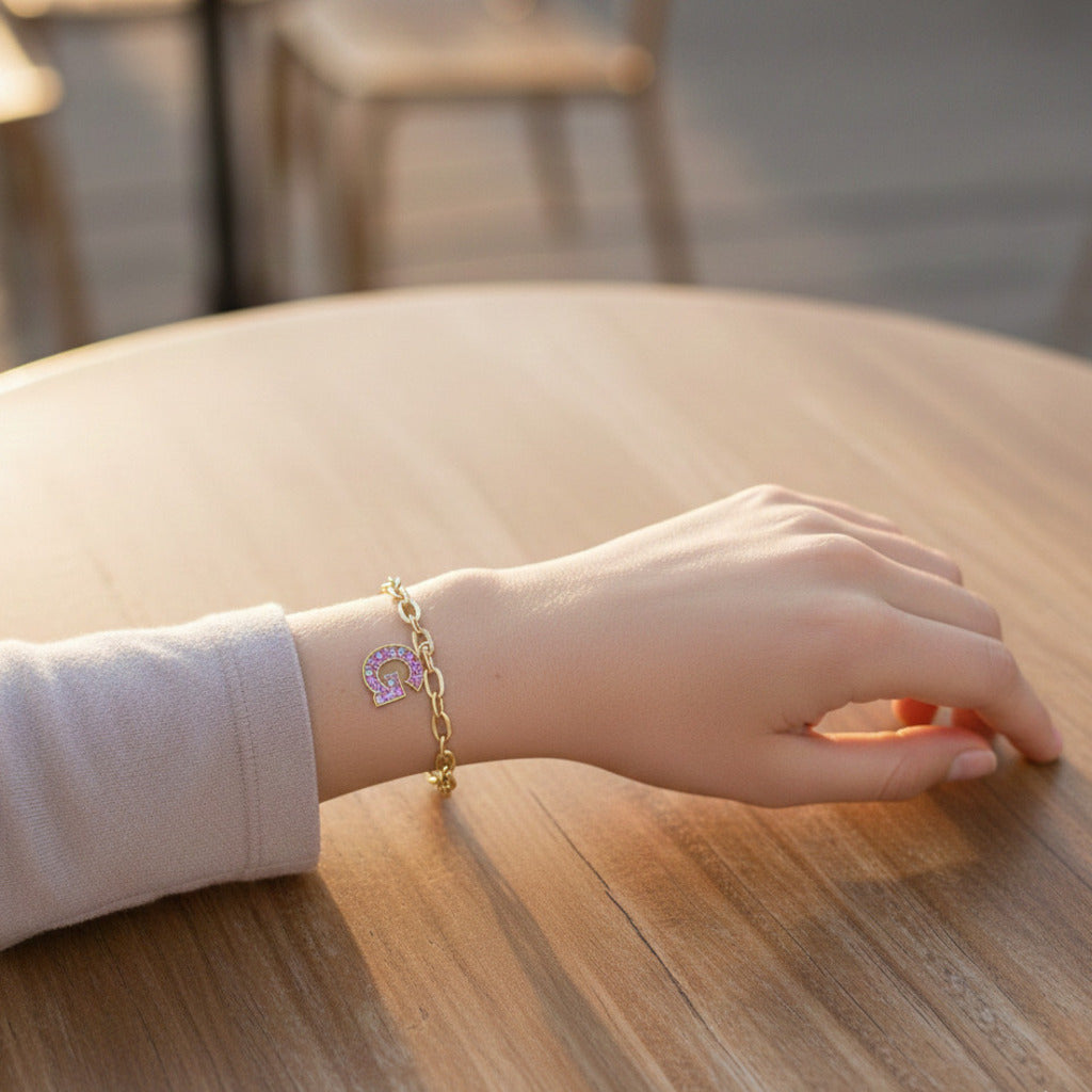 Hand with a letter G charm with a gold bracelet
