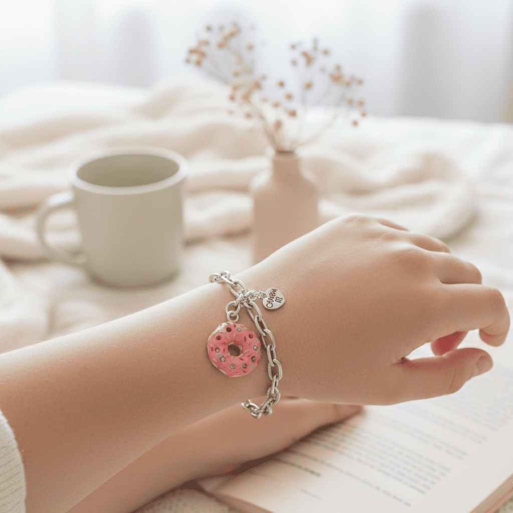 Hand wearing a bracelet with a pink donut charm on a soft, blurred background