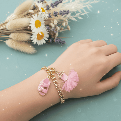 Hand wearing a gold bracelet with pink sandal charms on a light blue background with flowers.