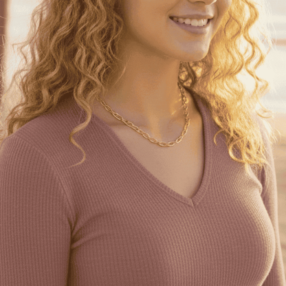 Woman wearing a pink sweater and gold chain necklace with a blurred background