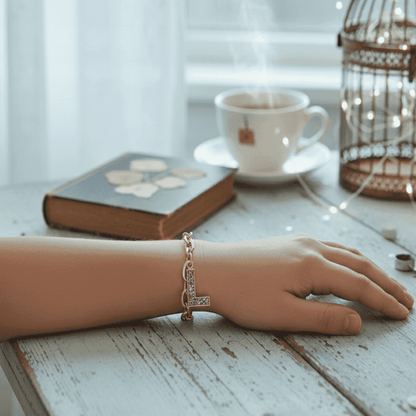 Hand wearing a bracelet on a wooden surface with a cup of tea and book in the background