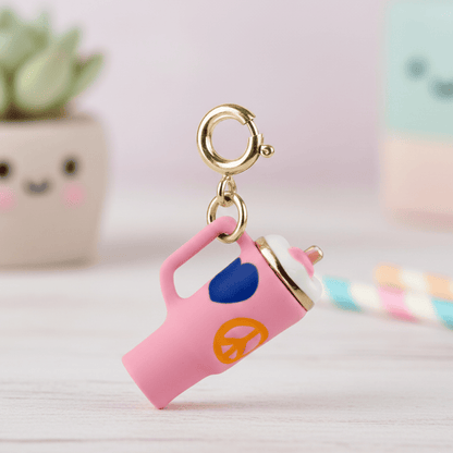 Pink teapot-shaped keychain with gold accents on a light surface.