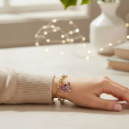 Hand wearing a gold bracelet with letter 'W' charms on a light surface.