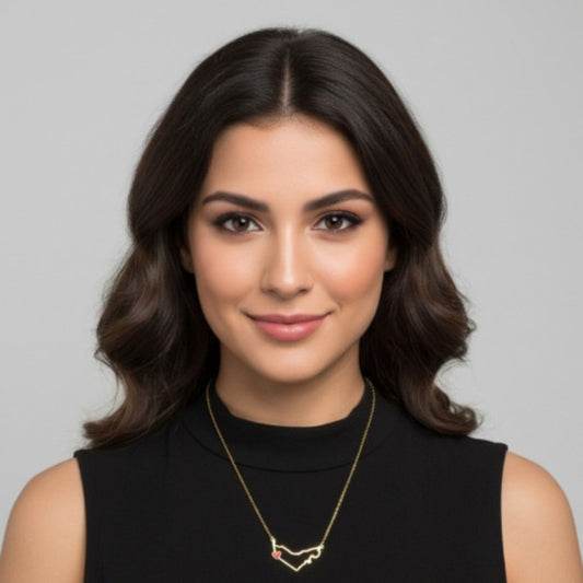 Woman wearing a black sleeveless top and gold necklace against a gray background