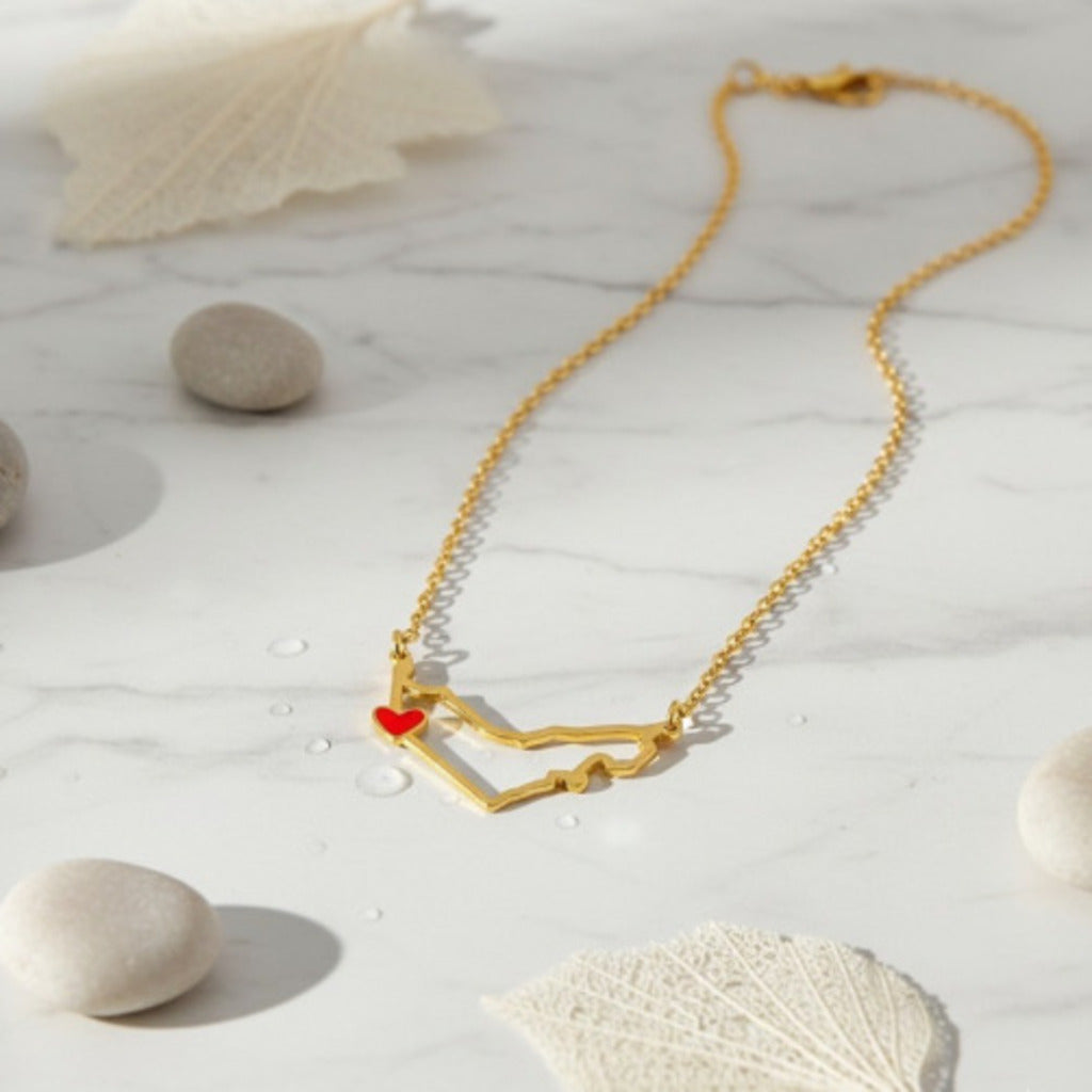 Gold necklace with a red heart pendant on a light background