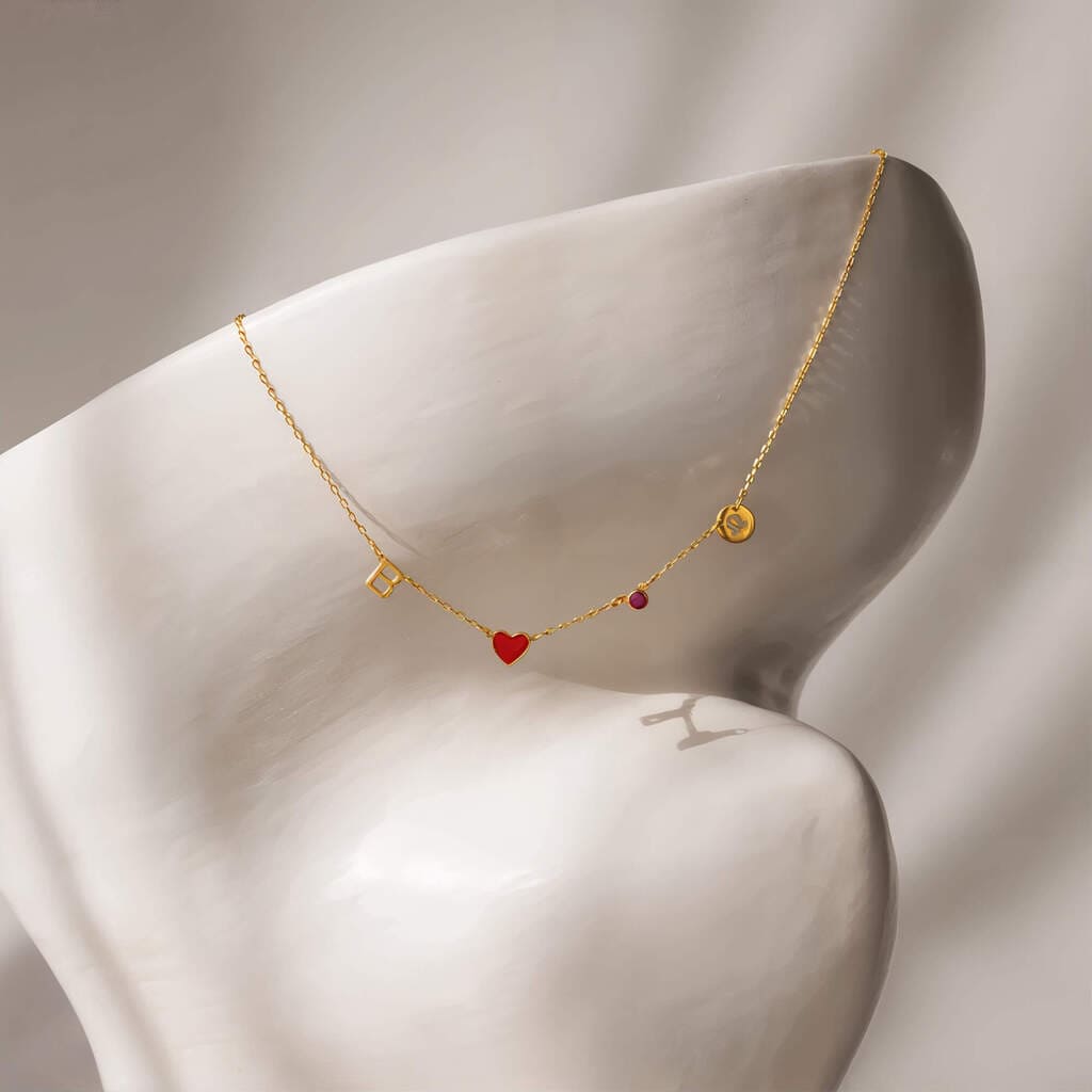 Gold necklace with heart and square charms on a mannequin bust against a neutral background