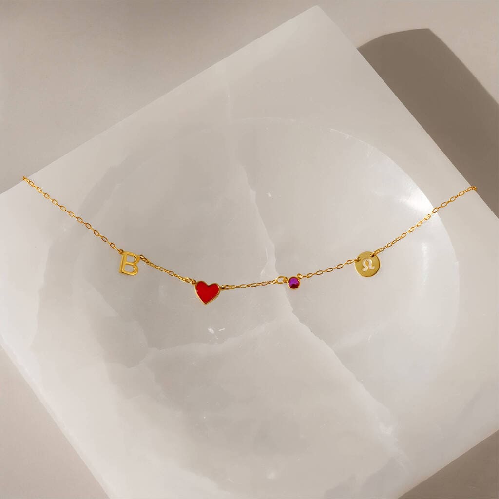 Gold bracelet with heart and round charm on a white stone surface