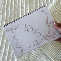 Calendar with '2025' design held by a hand on a textured white surface