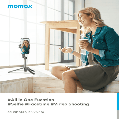 Woman using a smartphone with a selfie stick in a modern living room, featuring the momax brand.