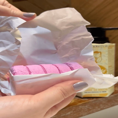 Pink rolled-up towel in tissue paper held by a hand on a wooden surface.