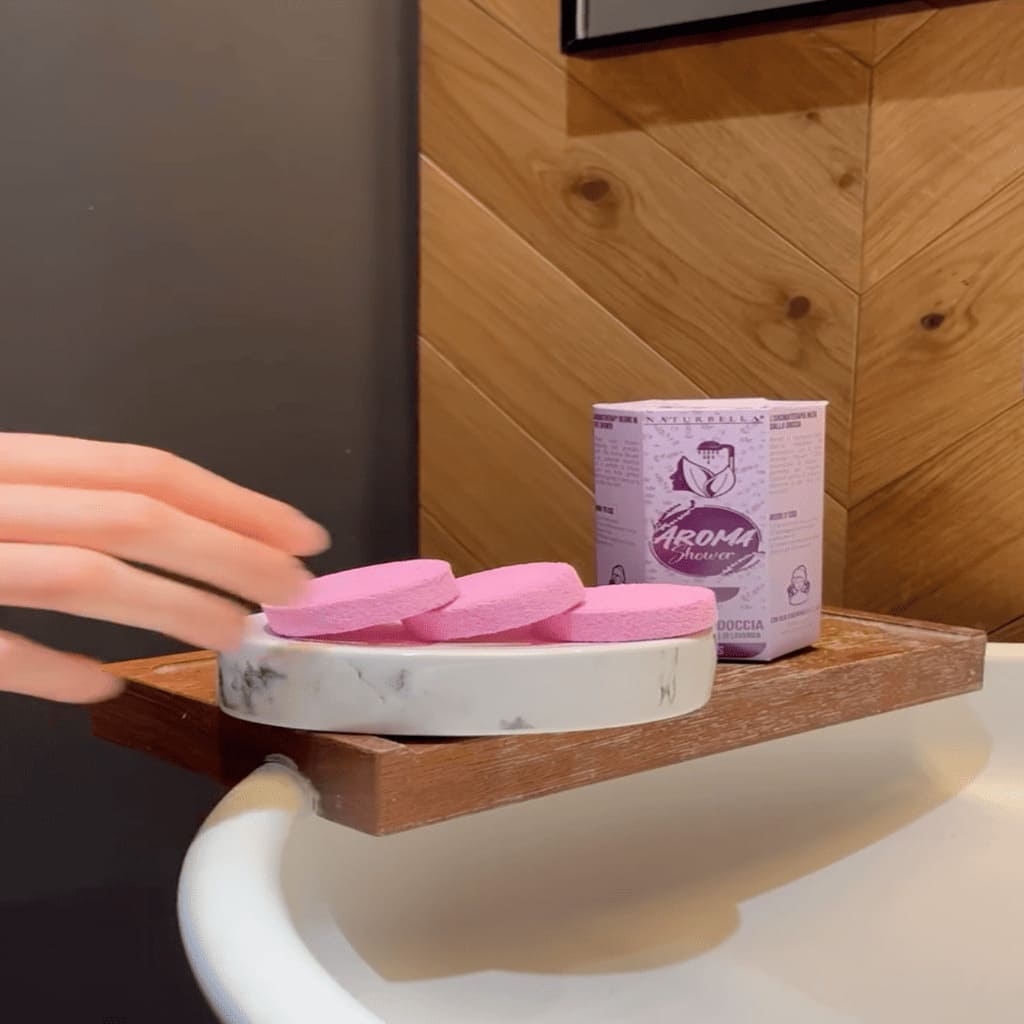 Pink soap bars on a marble soap dish with a purple box labeled 'Aroma' in a bathroom setting.