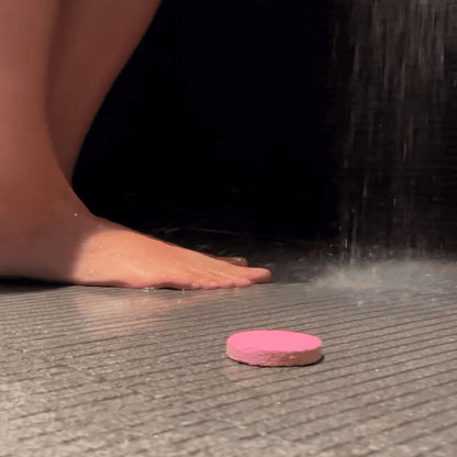Pink bath bomb on a tiled floor with water droplets and a shower in the background