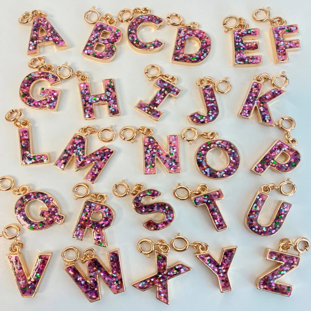 Gold letter charms with pink glittery letters on a white background