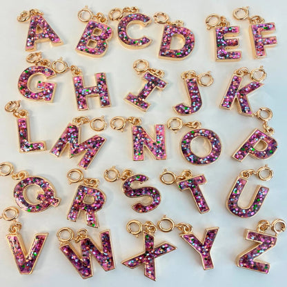 Gold letter charms with pink glittery letters on a white background