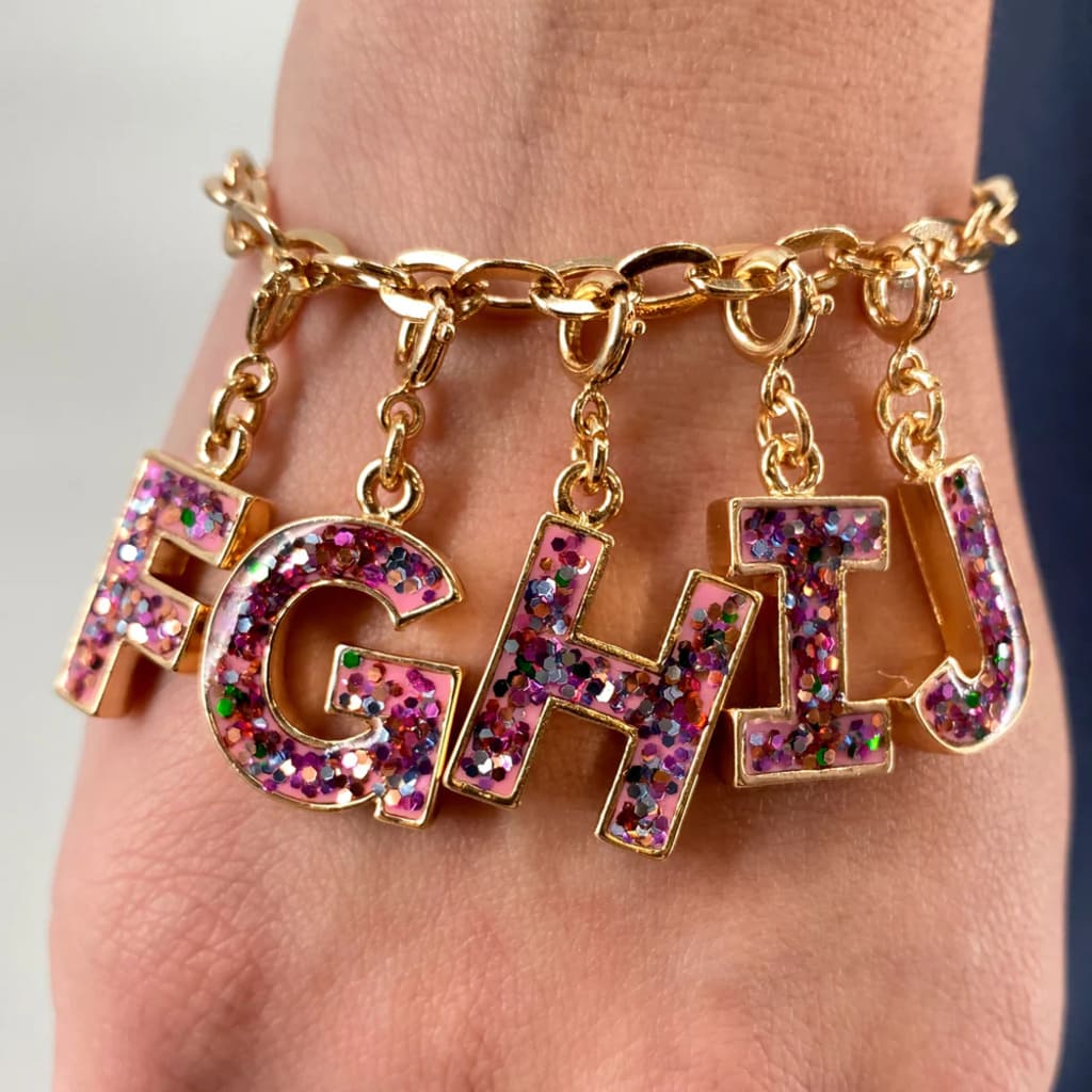 Gold bracelet with 'FGHT' charms on a wrist against a neutral background