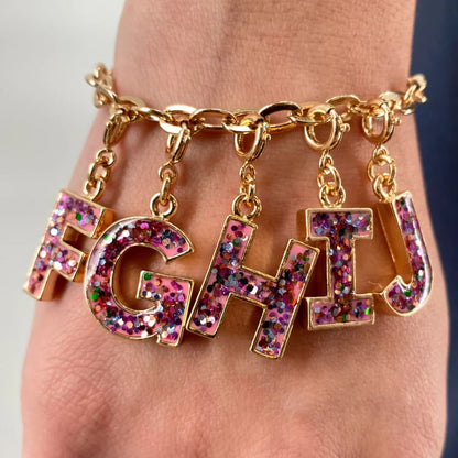 Gold bracelet with 'FGHT' charms on a wrist against a neutral background