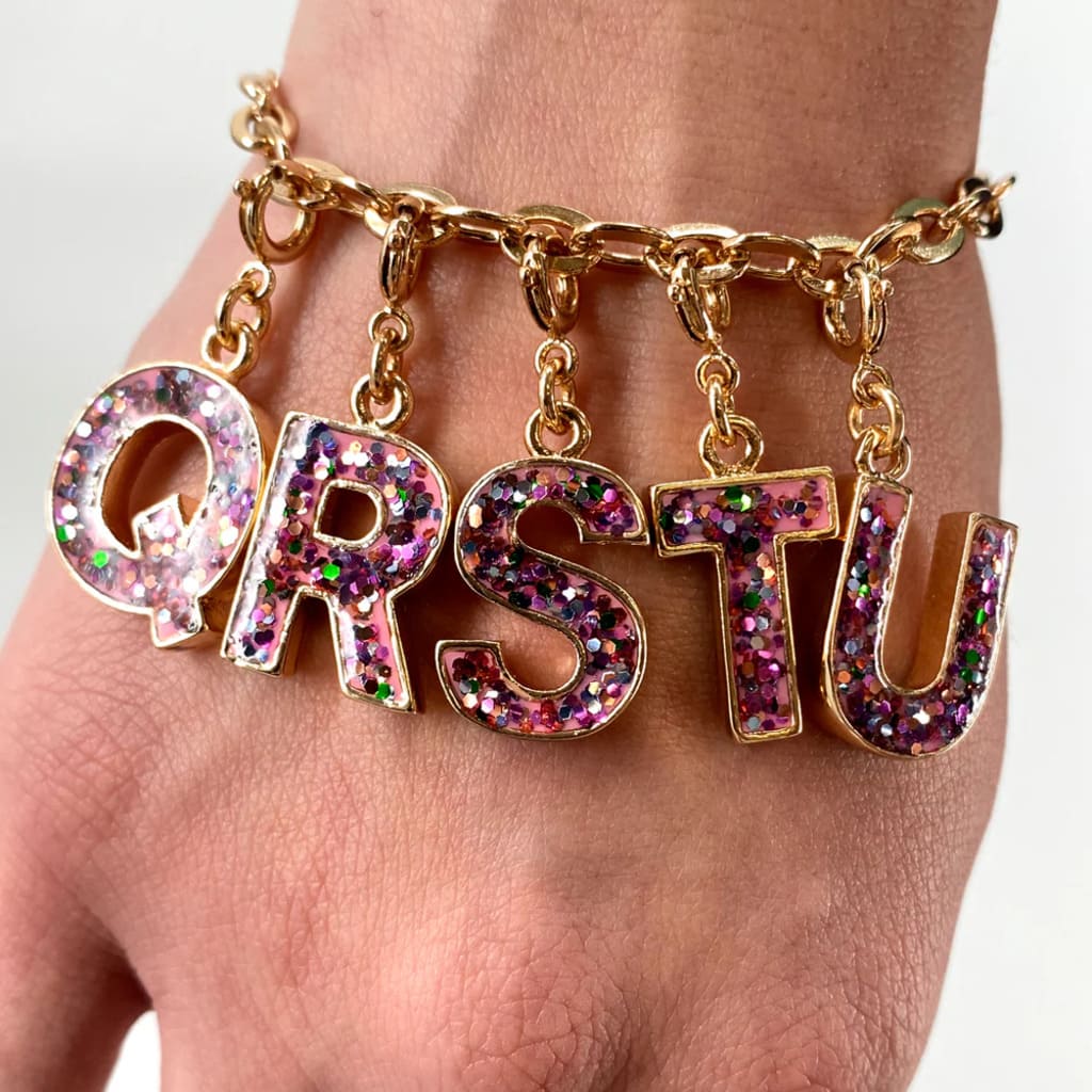 Gold bracelet with colorful letter charms on a wrist against a neutral background