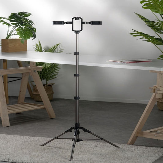 Black tripod stand with smartphone holder on a gray carpeted floor, surrounded by wooden furniture and plants.