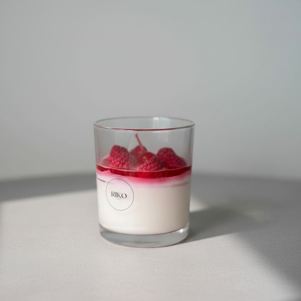 Candle in a glass container with raspberries on a gray background