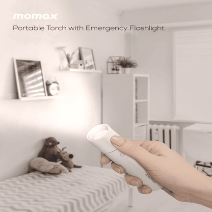 Hand holding a portable torch with emergency flashlight in a bedroom setting, with 'momax' branding.