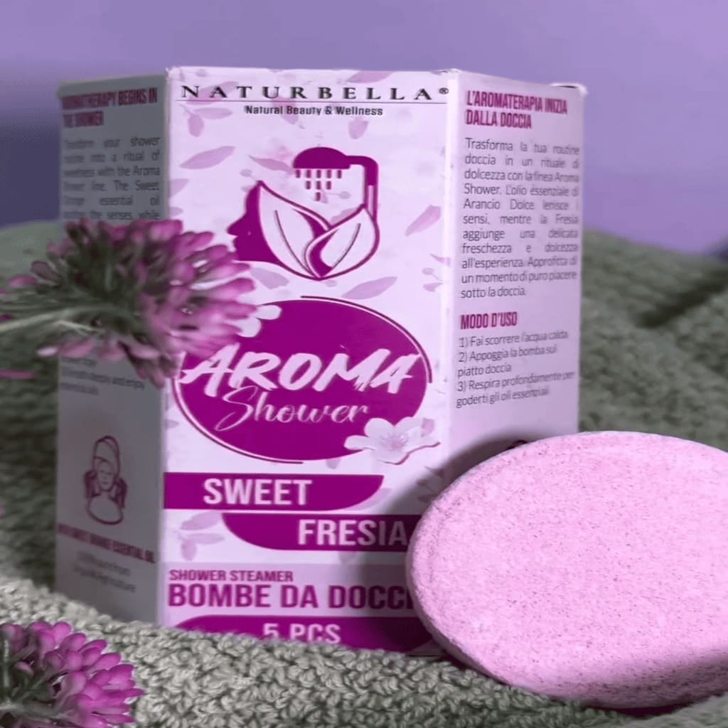 Naturbella Aroma Shower Sweet Fresia packaging with a pink shower steamer on a green surface.