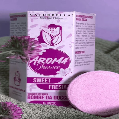 Naturbella Aroma Shower Sweet Fresia packaging with a pink shower steamer on a green surface.