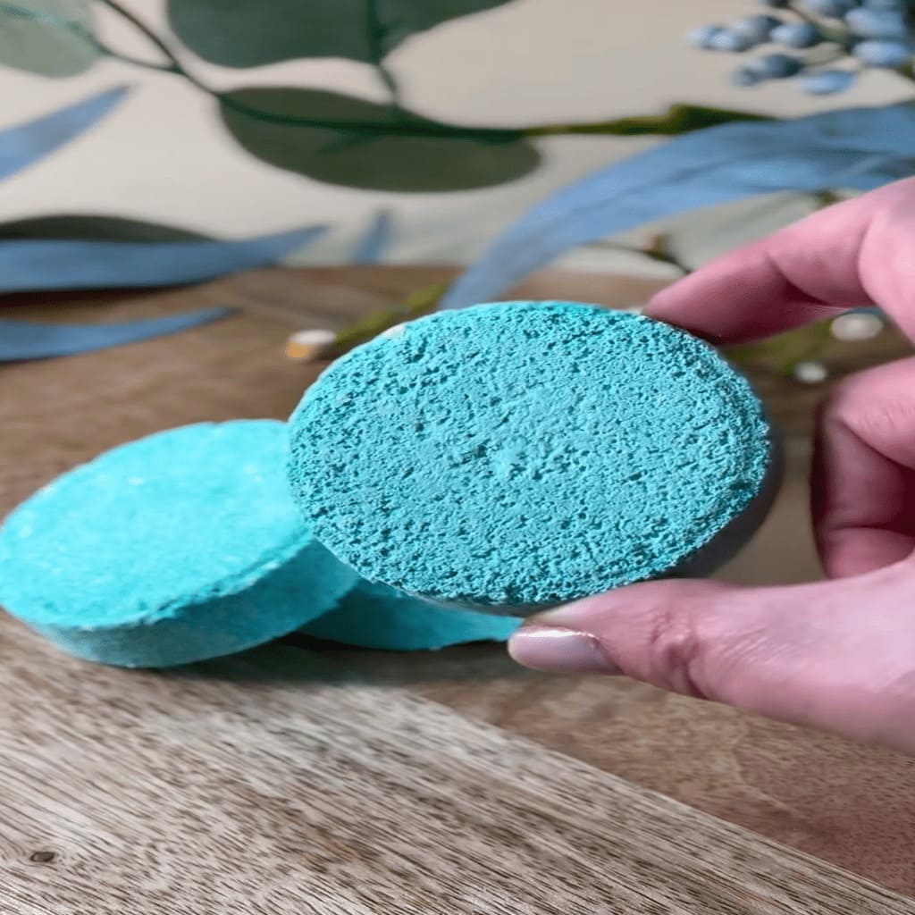 Turquoise konjac sponges held by a hand on a wooden surface with decorative elements.