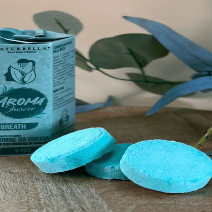 Blue bath bombs with a box labeled 'Aroma Shower' on a wooden surface with plants in the background.