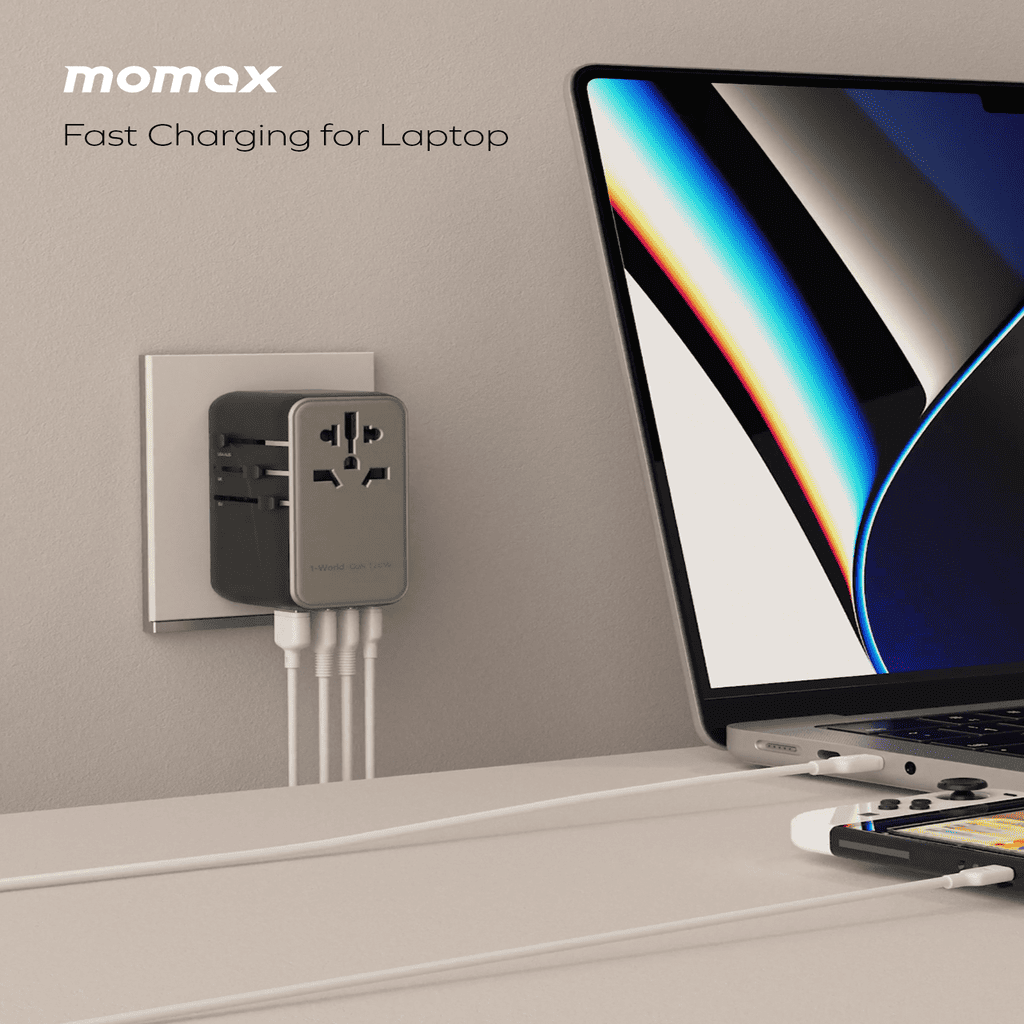 Momax laptop charger plugged into a wall socket with a laptop on a desk.