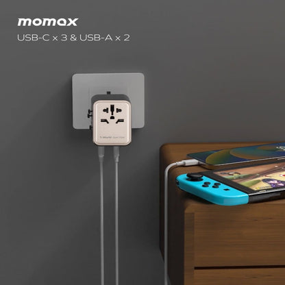 Momax wall adapter with multiple USB ports charging a phone and gaming console on a wooden surface.