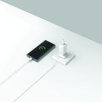 Phone charging via a power bank on a white surface with a gray background