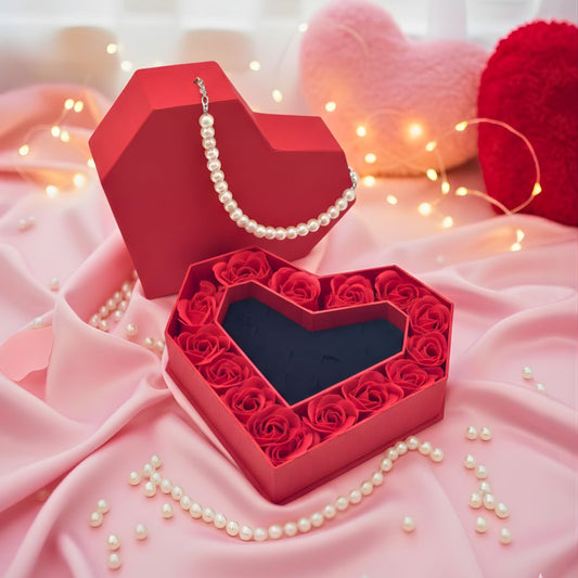 Heart-shaped red box filled with red roses on a pink fabric background with pearls.