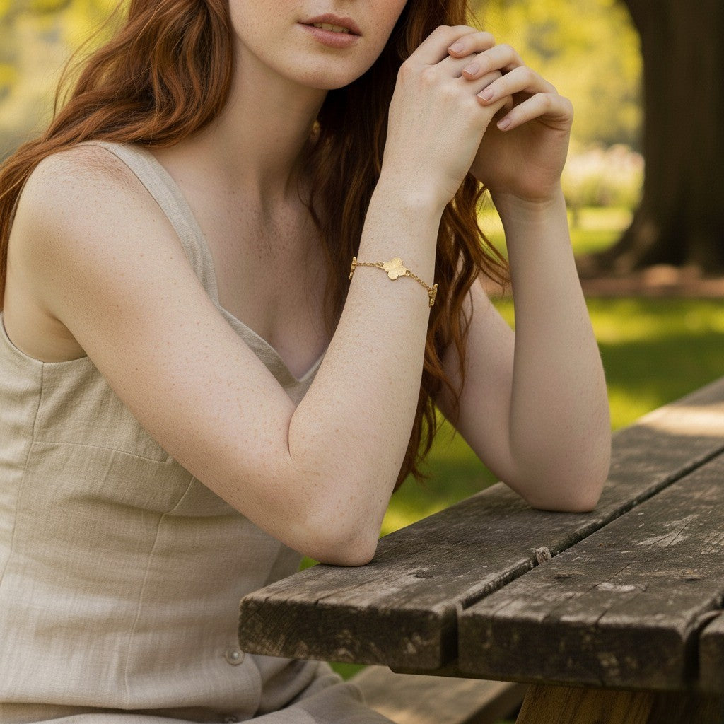 Woman sitting at a wooden table in a park, wearing a gold bracelet.
