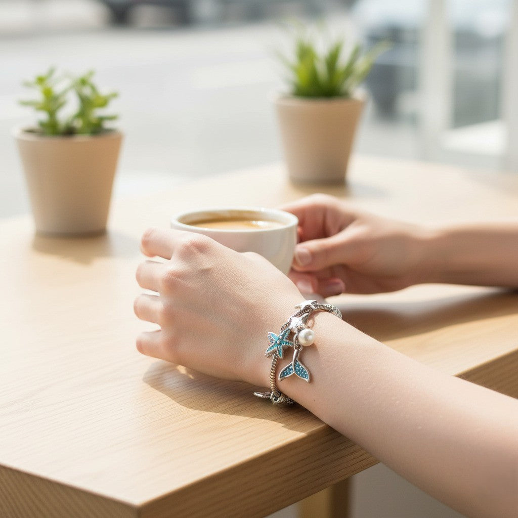 Person's hand wearing a bracelet with a cup of coffee on a table with plants in the background