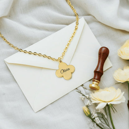 Gold necklace with a name pendant on a white envelope with flowers and a stamp.