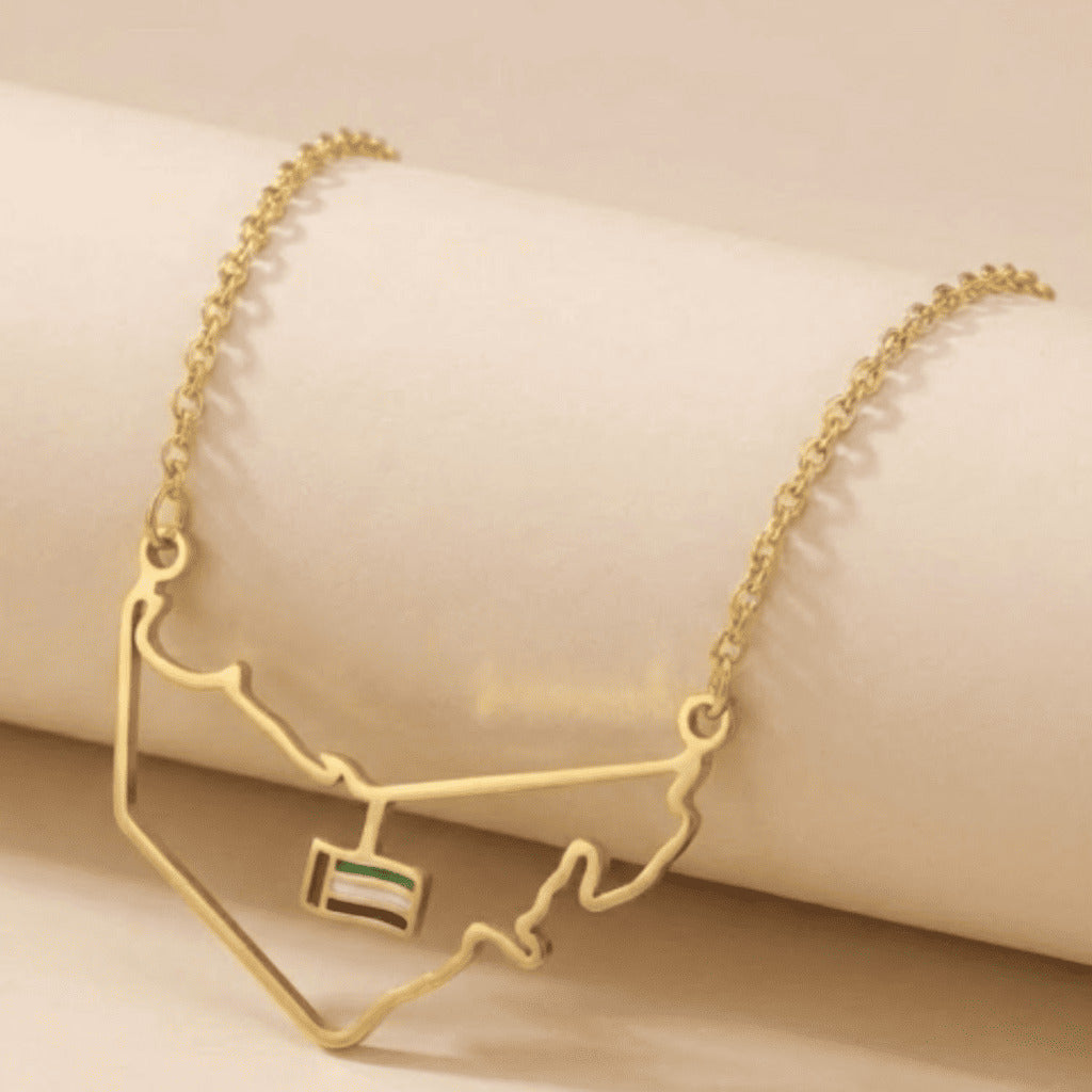 Gold necklace with a map design and small flag pendant on a beige background