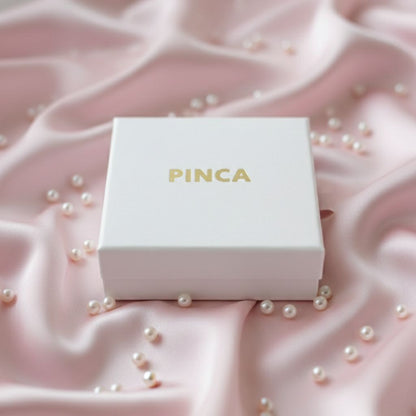 PINCA jewelry box on a pink fabric background with scattered pearls